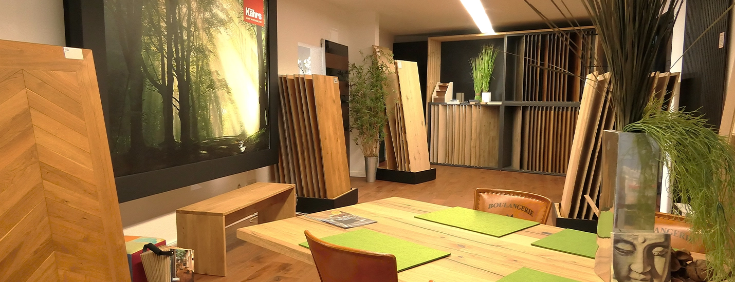 Showroom mit verschiedenen Holzboden-Musterplatten und Dielen, im Vordergrund ein Holztisch mit grünen Sitzkissen